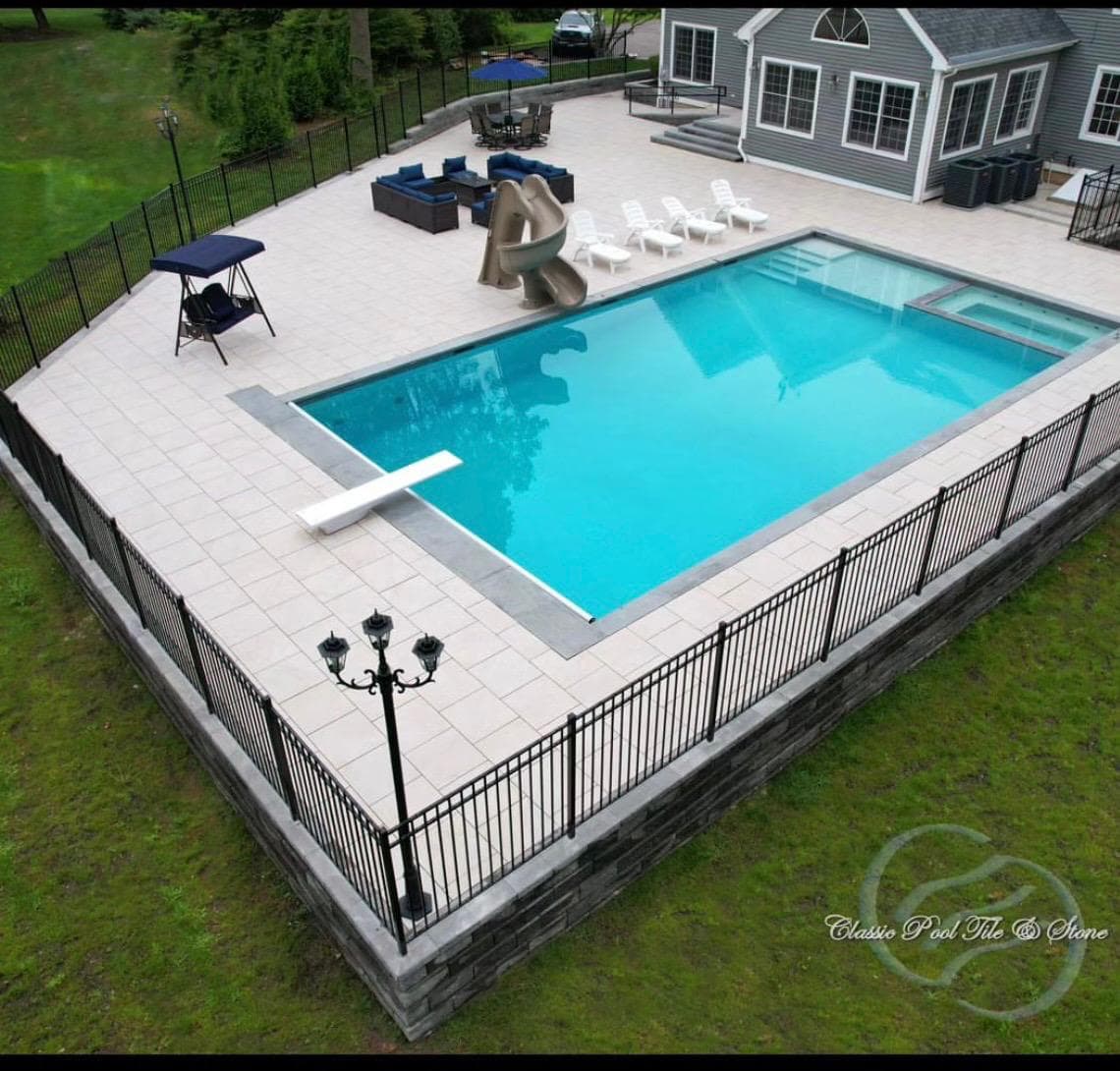 Backyard pool enclosed by black aluminum fencing on a stone-veneer base