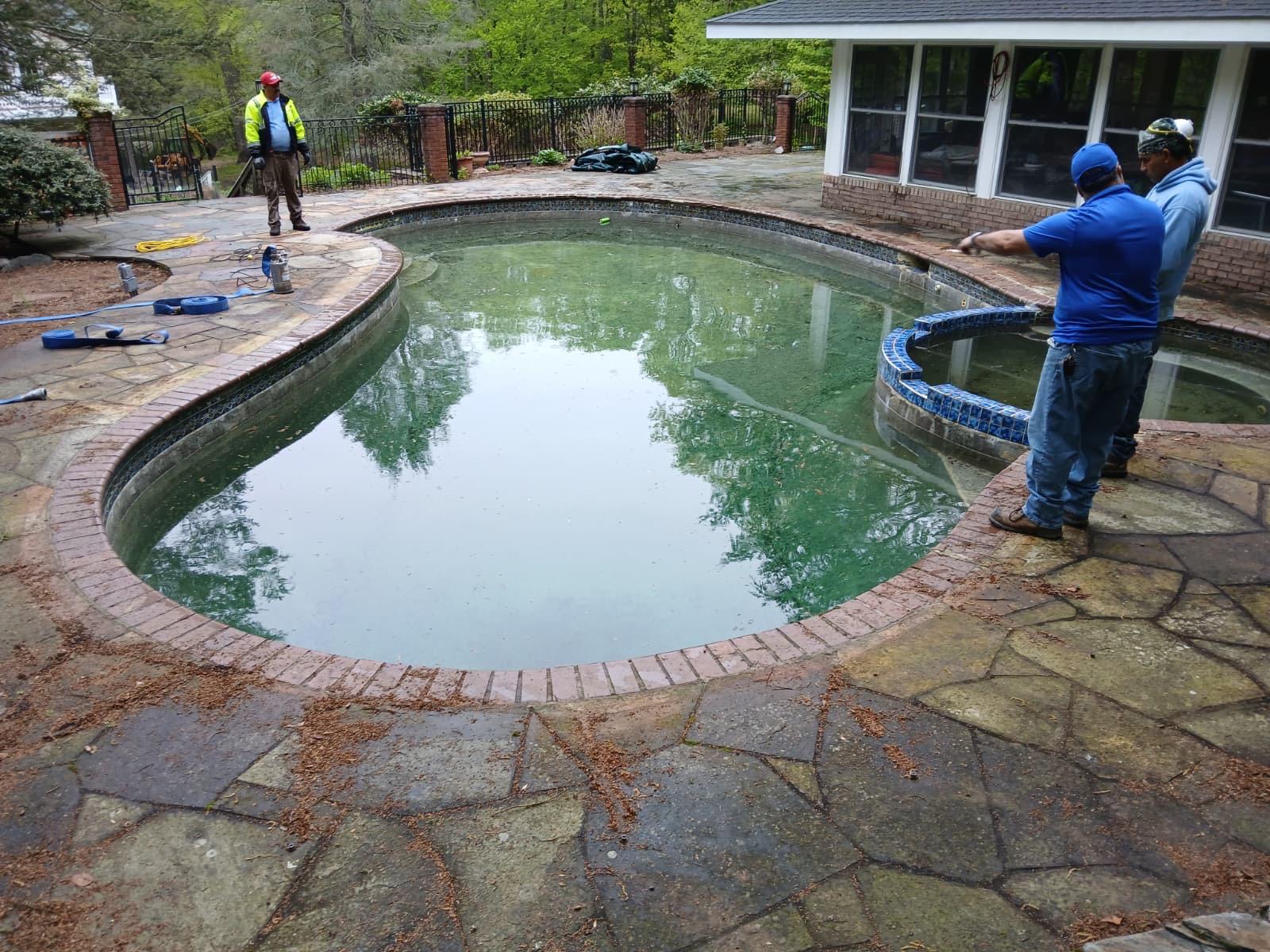 Green, algae-filled pool with a service crew on-site, the starting point before renovation
